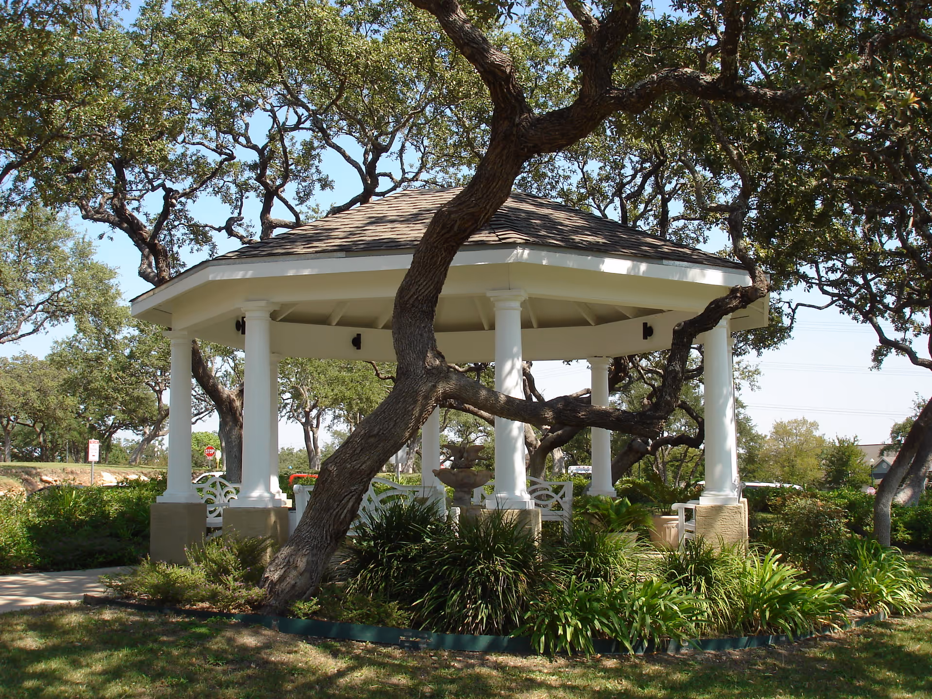 A white octagonal gazebo with columns nestled among oak trees and landscaped greenery.