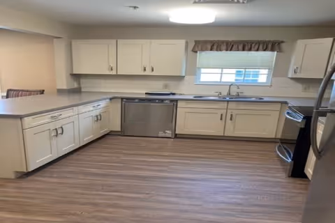 Spacious kitchen with white cabinets, stainless steel appliances, a sink under a window, and wood-look flooring.