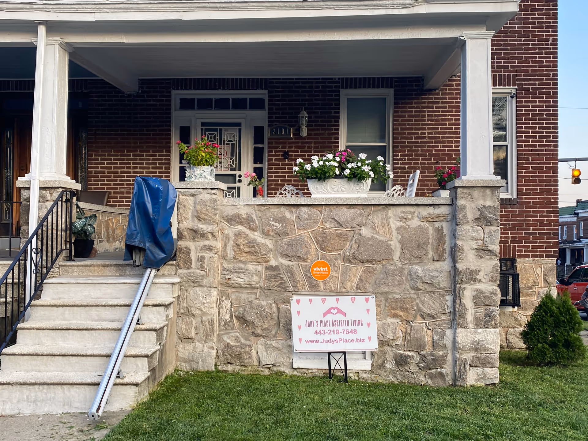 Stone-front brick house with a covered porch and a lawn sign reading Judy's Place Assisted Living.
