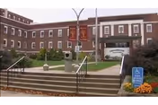 Brick elder care facility facade with steps, accessible ramp, wheelchair sign, banners, and manicured landscaping.