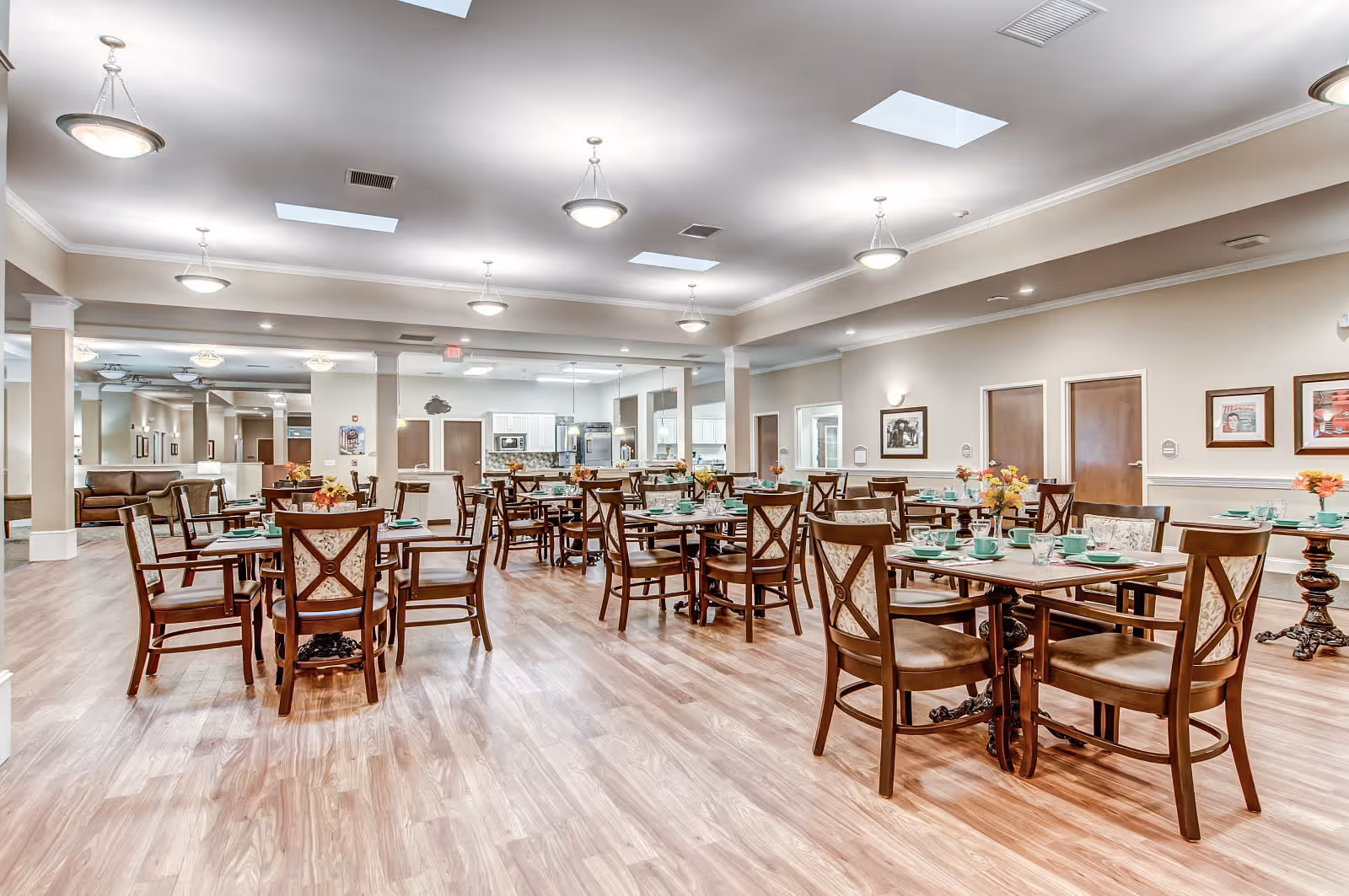 Spacious furnished dining room with multiple tables and chairs set for meals in a senior living facility.