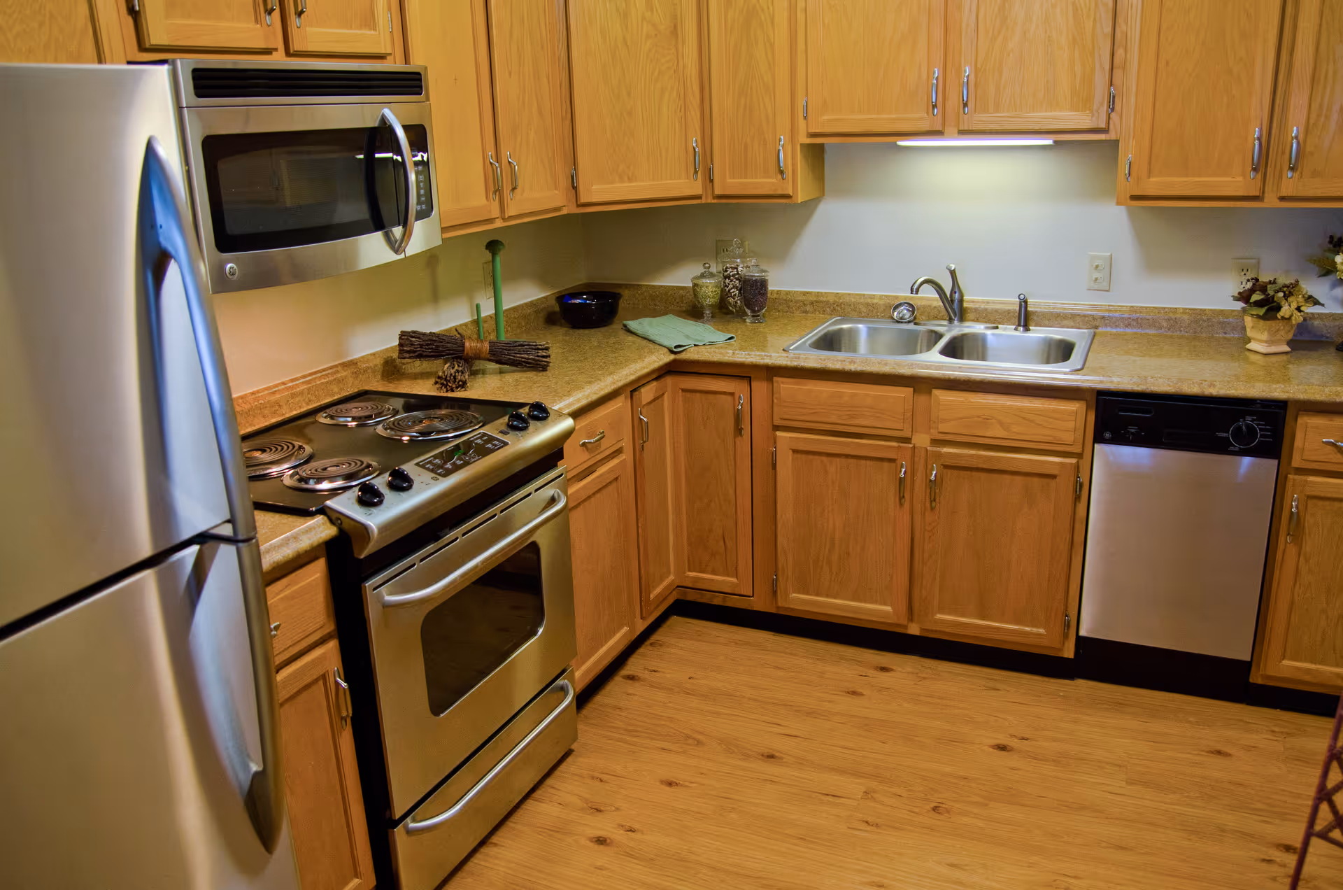 Kitchen with stainless steel refrigerator, stove, microwave, dishwasher, wooden cabinets, and a double sink.