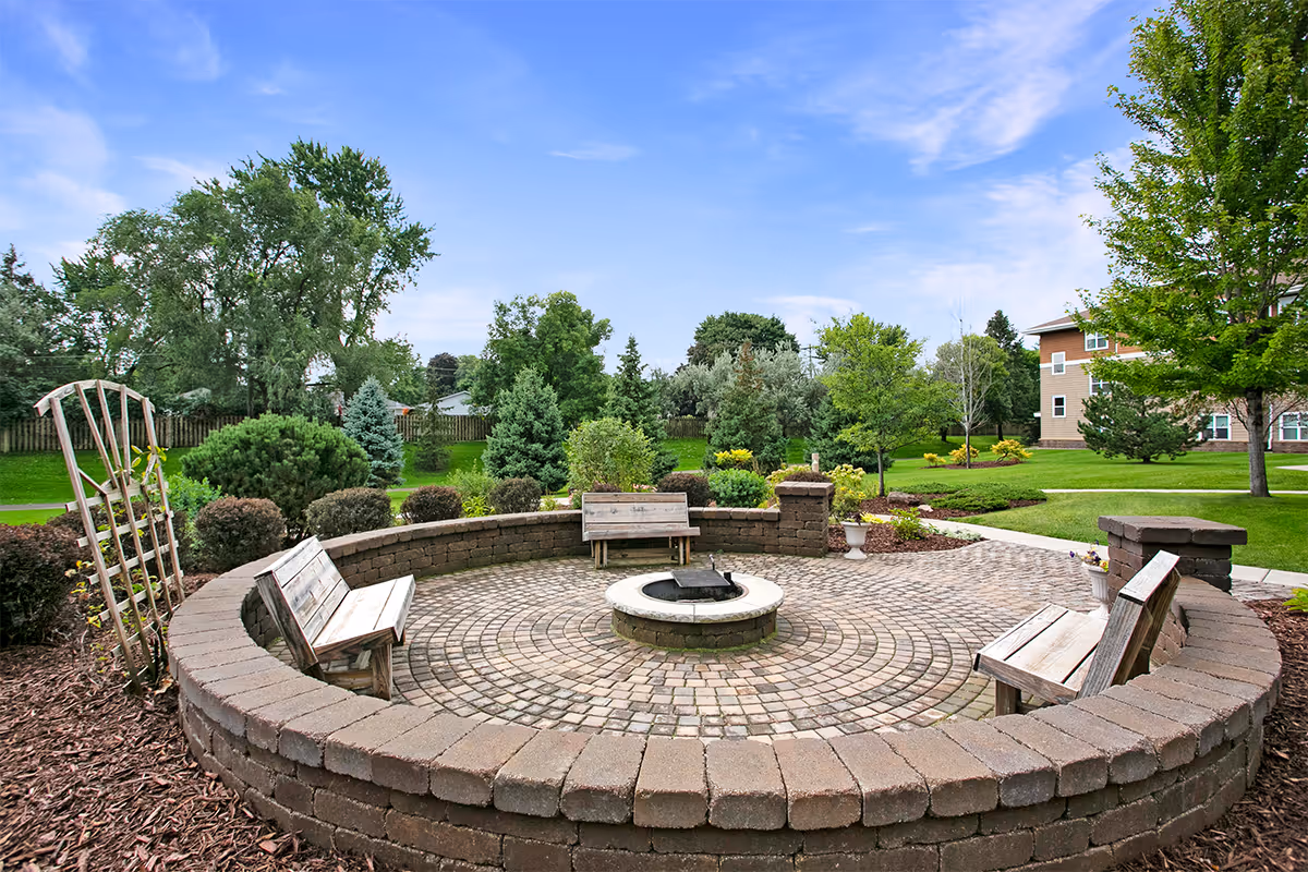 Circular brick patio with wooden benches around a central fire pit in a landscaped courtyard.