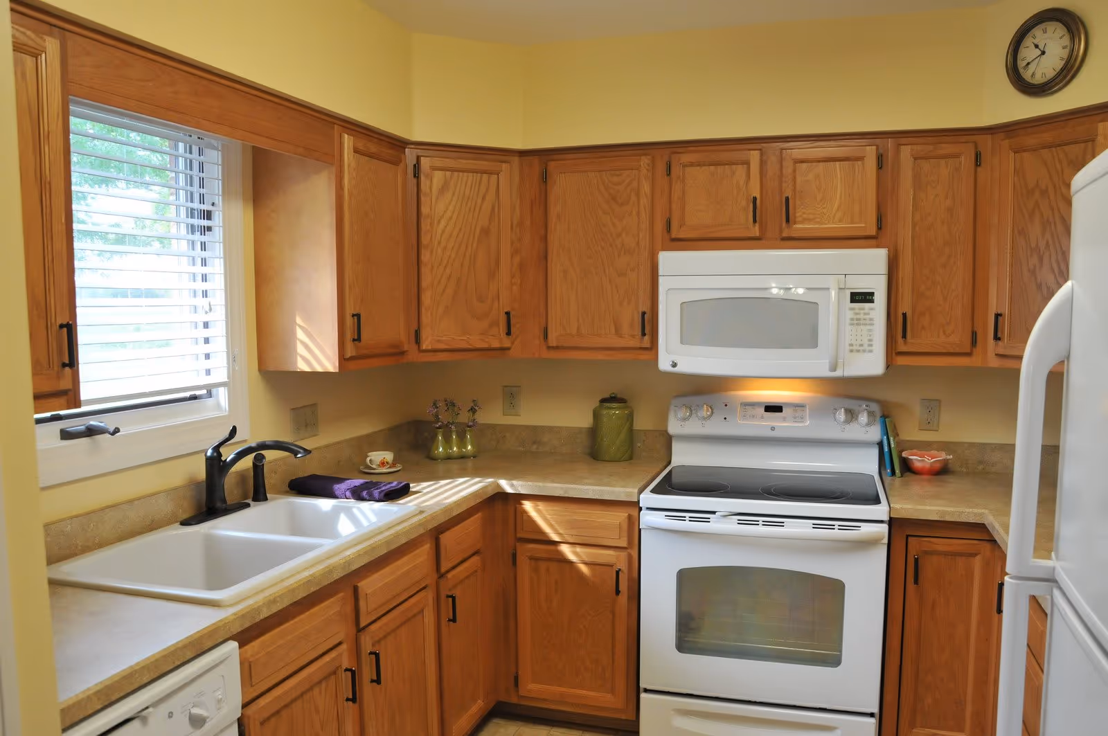 Bright kitchen with oak cabinets, a white stove and microwave, a sink under a window, and a refrigerator.