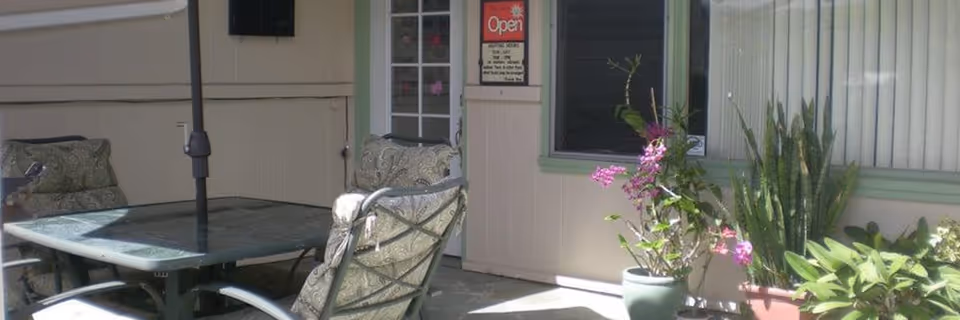 Outdoor patio with glass-top table, chairs, and potted plants outside a building.