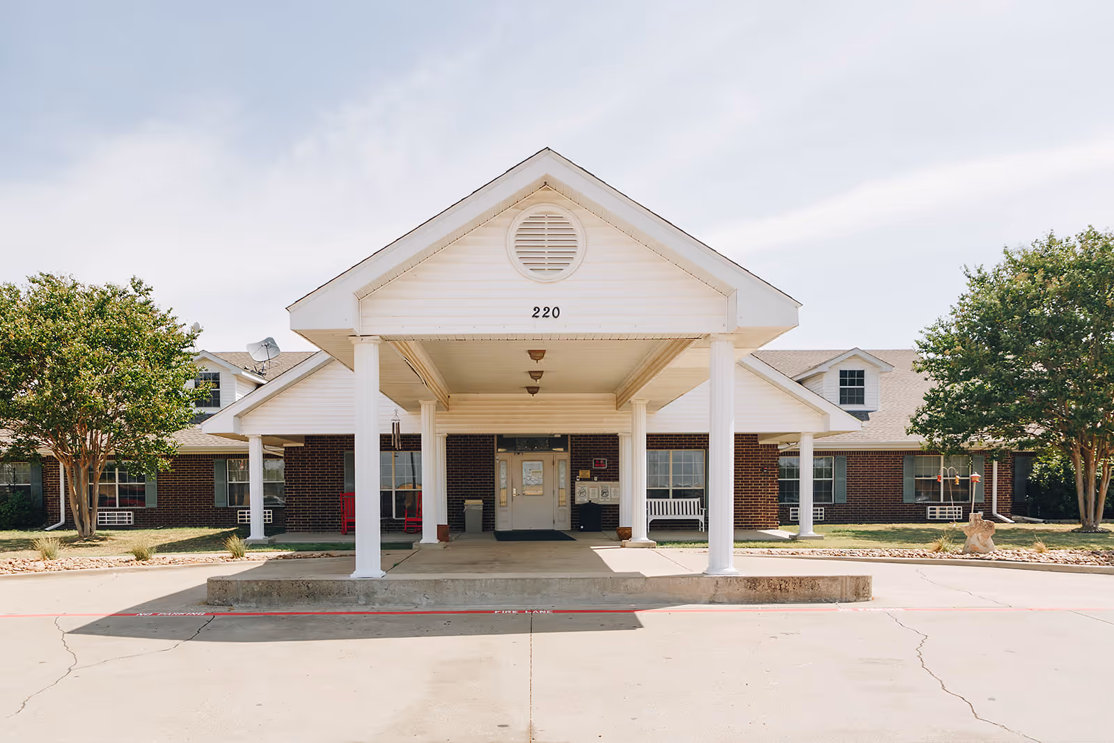 Front exterior view of Renaissance Rehabilitation and Healthcare Center showing a covered entrance with white columns, a brick building facade, and two trees on either side.