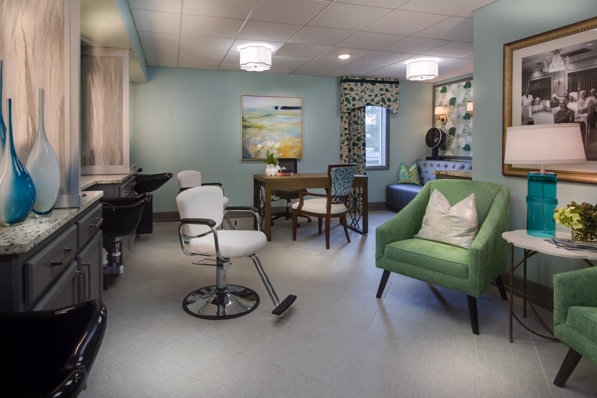 A mint-green interior salon and sitting area with styling chairs, a table, and comfortable green armchairs.