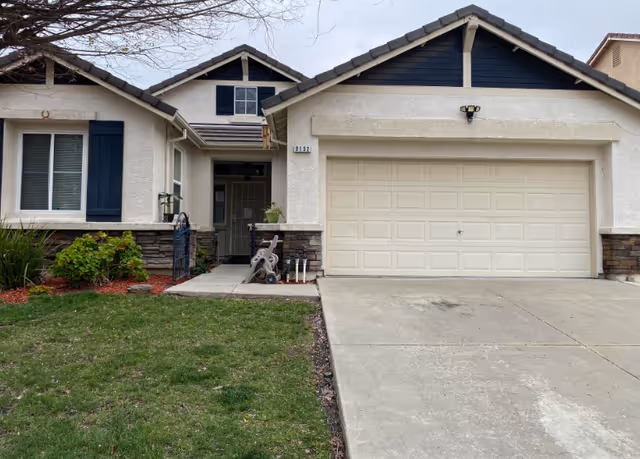Front exterior of a beige single-story house with an attached two-car garage, driveway, front lawn, and covered entry.