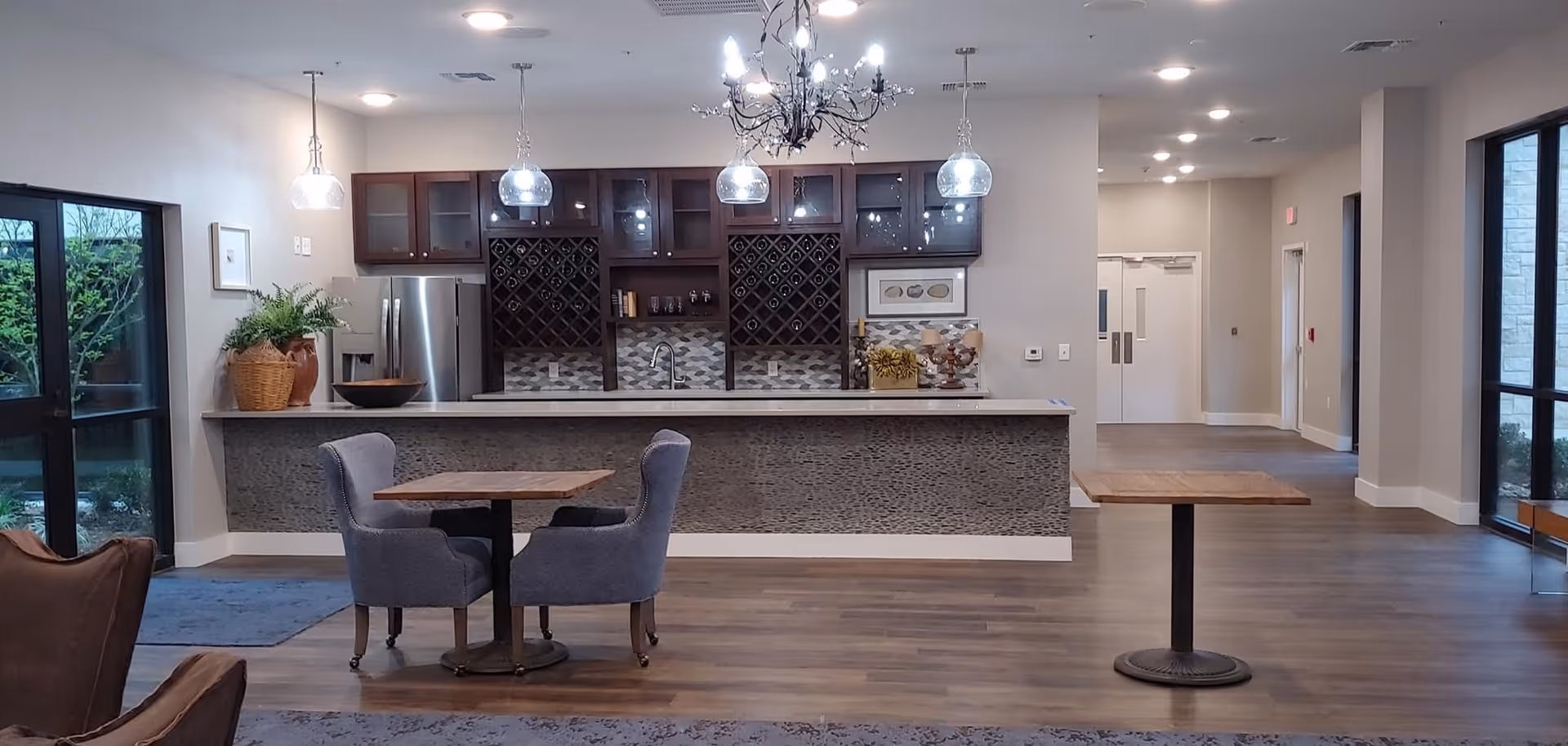 Spacious interior common area with a countertop bar and cabinetry, pendant lights, and small tables with upholstered chairs.