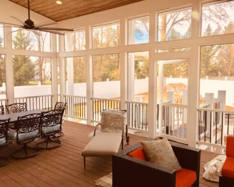 Sunroom-style living area with lounge seating, a dining table, and large floor-to-ceiling windows overlooking a fenced yard.