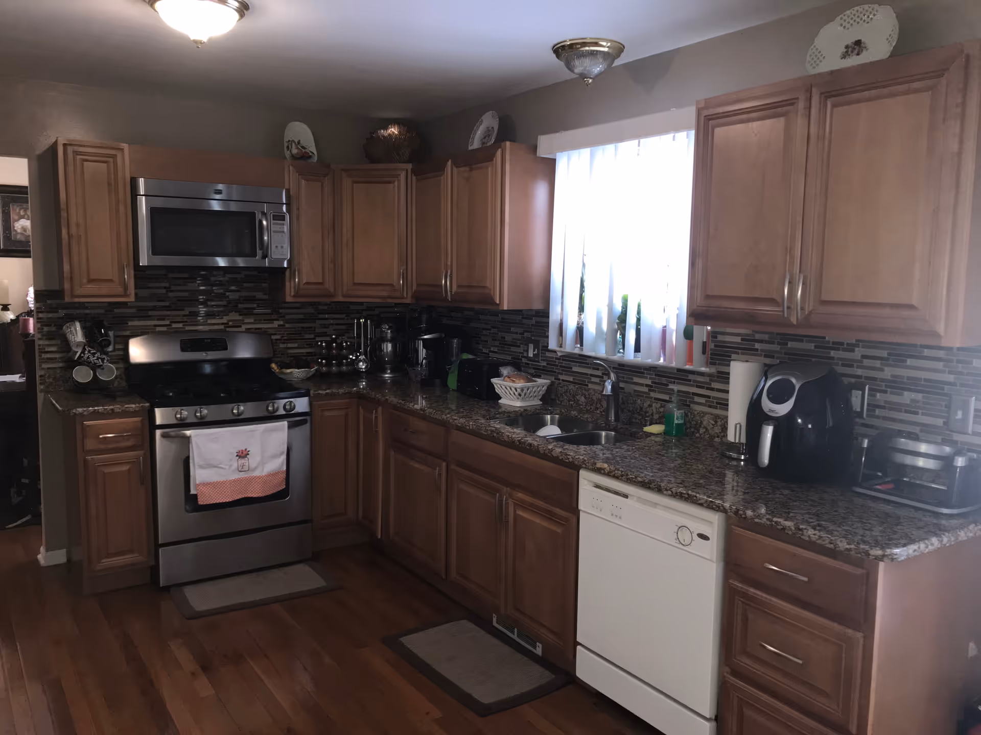Kitchen with wooden cabinets, granite countertops, a stainless steel stove and microwave, dishwasher, sink, and small appliances.