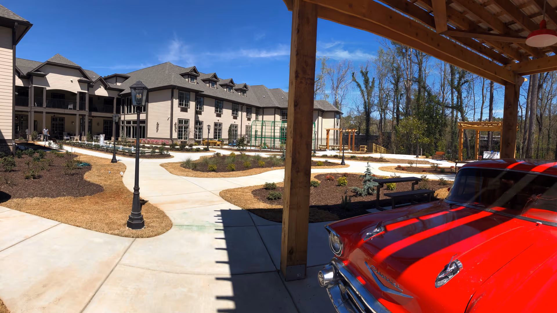 Outdoor courtyard of Orchard at Brookhaven showing walkways, landscaped beds, a multi-story building, and a red vintage car under a wooden canopy.