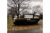 Outdoor view of a sign for Cortland Park Rehabilitation And Nursing Center surrounded by trimmed bushes and leafless trees on a cloudy day.