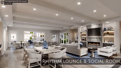 A spacious and modern lounge and social room with multiple seating areas including a large dining table with chairs, sofas, and armchairs arranged around a fireplace with a mounted flat-screen TV above it. The room has large windows and glass doors letting in natural light, light-colored walls and ceiling with recessed lighting, and decorative shelves with books and ornaments.