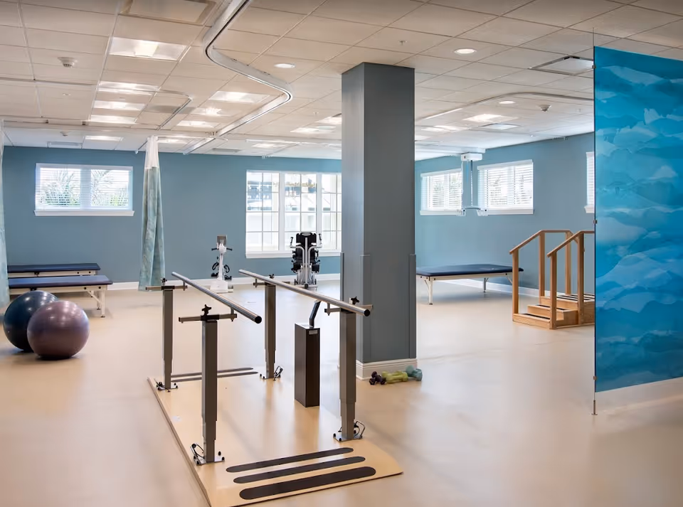 Rehabilitation gym with parallel bars, therapy stairs, exercise balls, and treatment benches in a bright room.