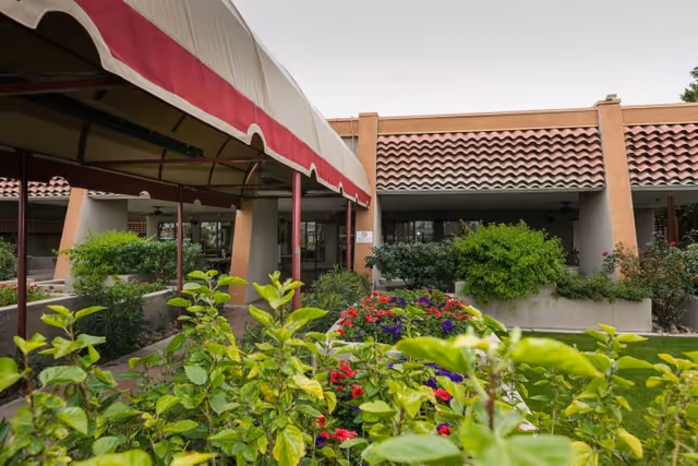 Entrance courtyard with a covered walkway, tiled roof, and colorful flowerbeds in front of the building.
