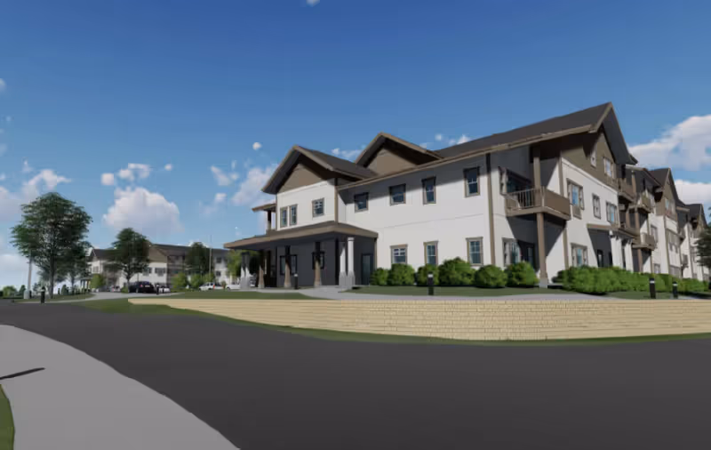 Exterior rendering of a multi-story senior living building with a covered entrance, balconies, landscaped grounds, and a driveway under a blue sky.