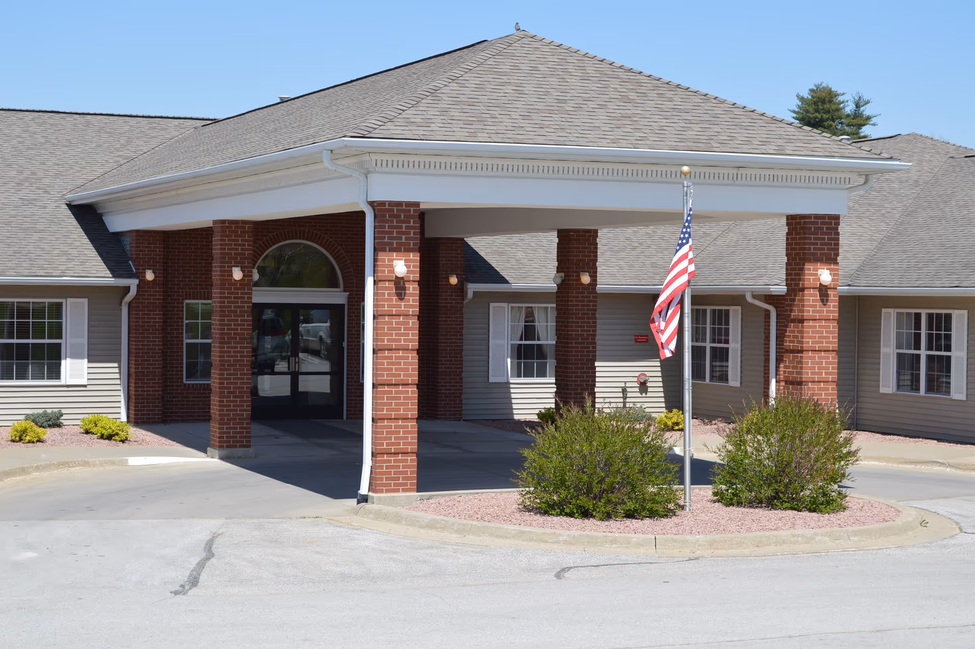 Front entrance of Crestview Specialty Care with a covered porte-cochere supported by brick columns and an American flag in front.