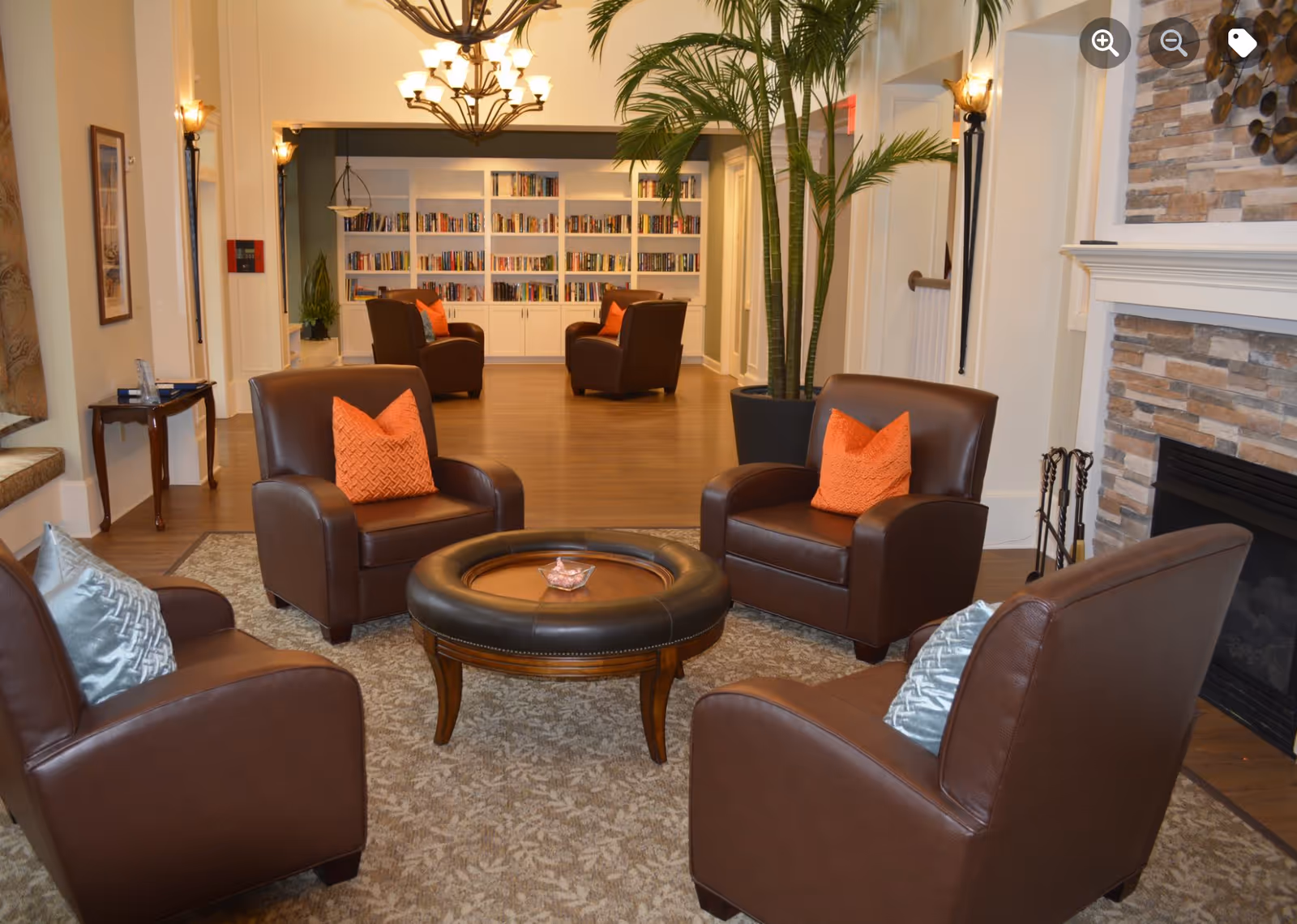 Cozy lounge with four brown leather chairs arranged around a round ottoman, a fireplace, and bookshelves in the background.