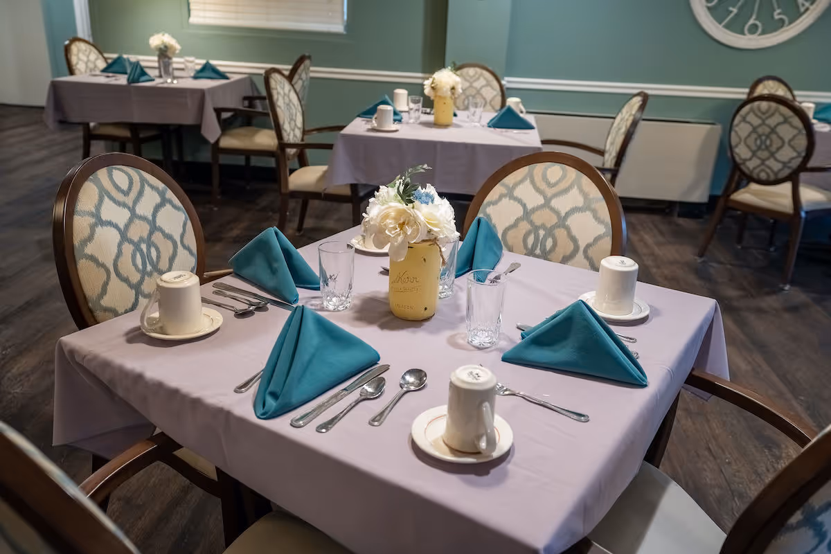 Table set with teal napkins, cups, utensils, and a floral centerpiece in a dining room.