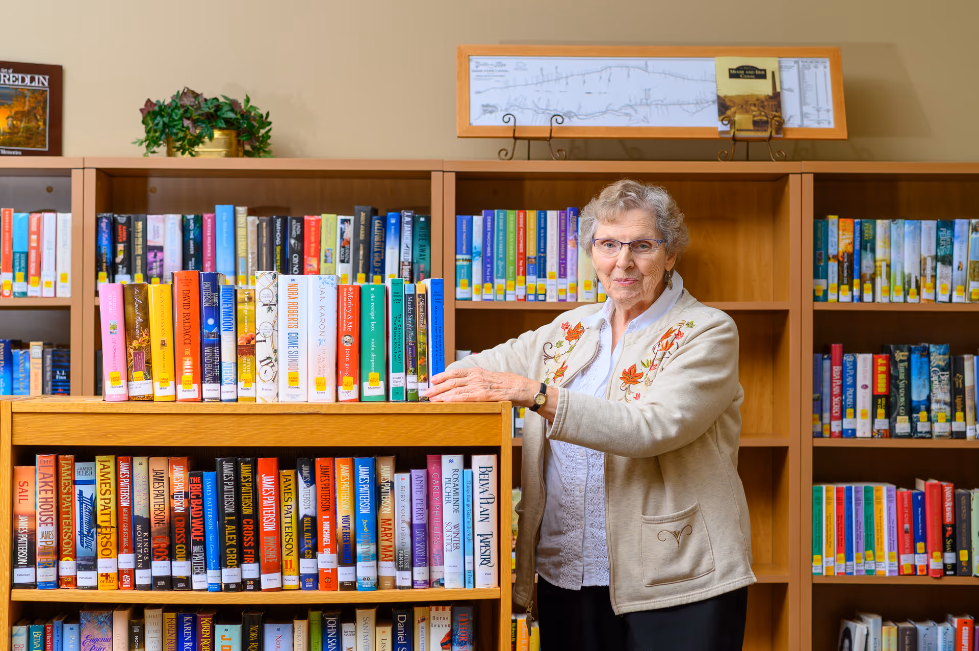 A woman stands beside wooden bookshelves filled with books in a library-like interior.