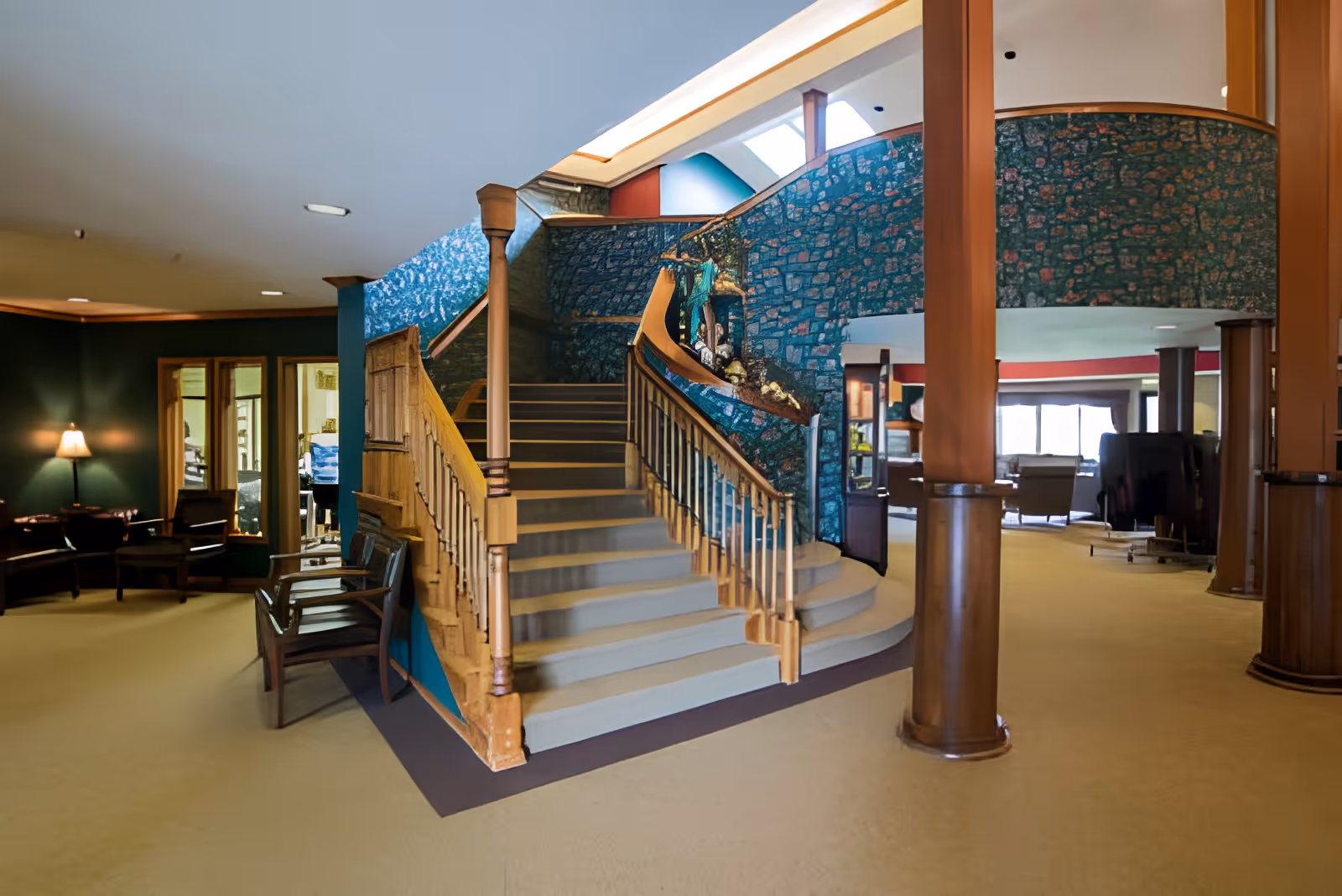 A spacious interior lobby with a central curved wooden staircase, seating areas, and decorative patterned walls.