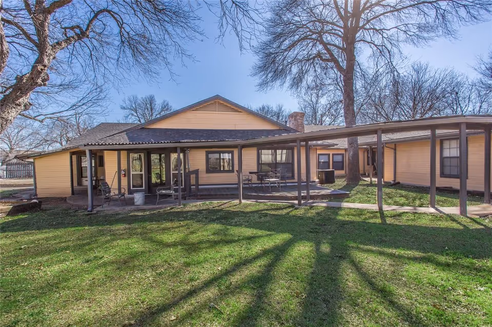 Exterior view of a single-story yellow building with a covered porch and walkway overlooking a grassy yard.