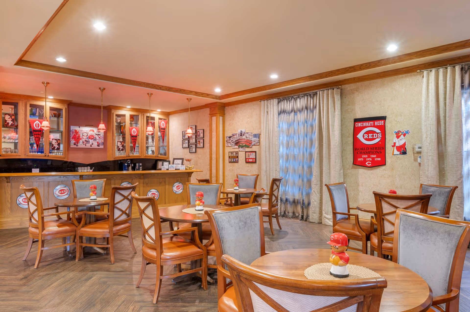 A cozy dining/lounge area with round wooden tables and chairs, a small bar, and Cincinnati Reds memorabilia on the walls.