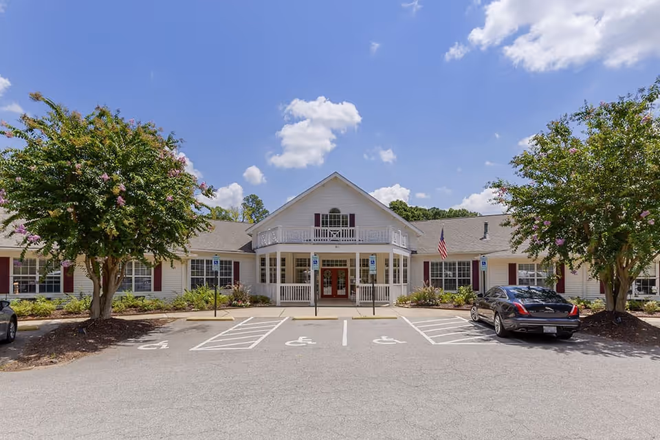 Front exterior of a single-story senior living building with a central entrance, balcony, and handicap parking spaces.
