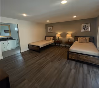 Two twin beds with nightstands and lamps in a spacious senior living bedroom, near a bathroom.