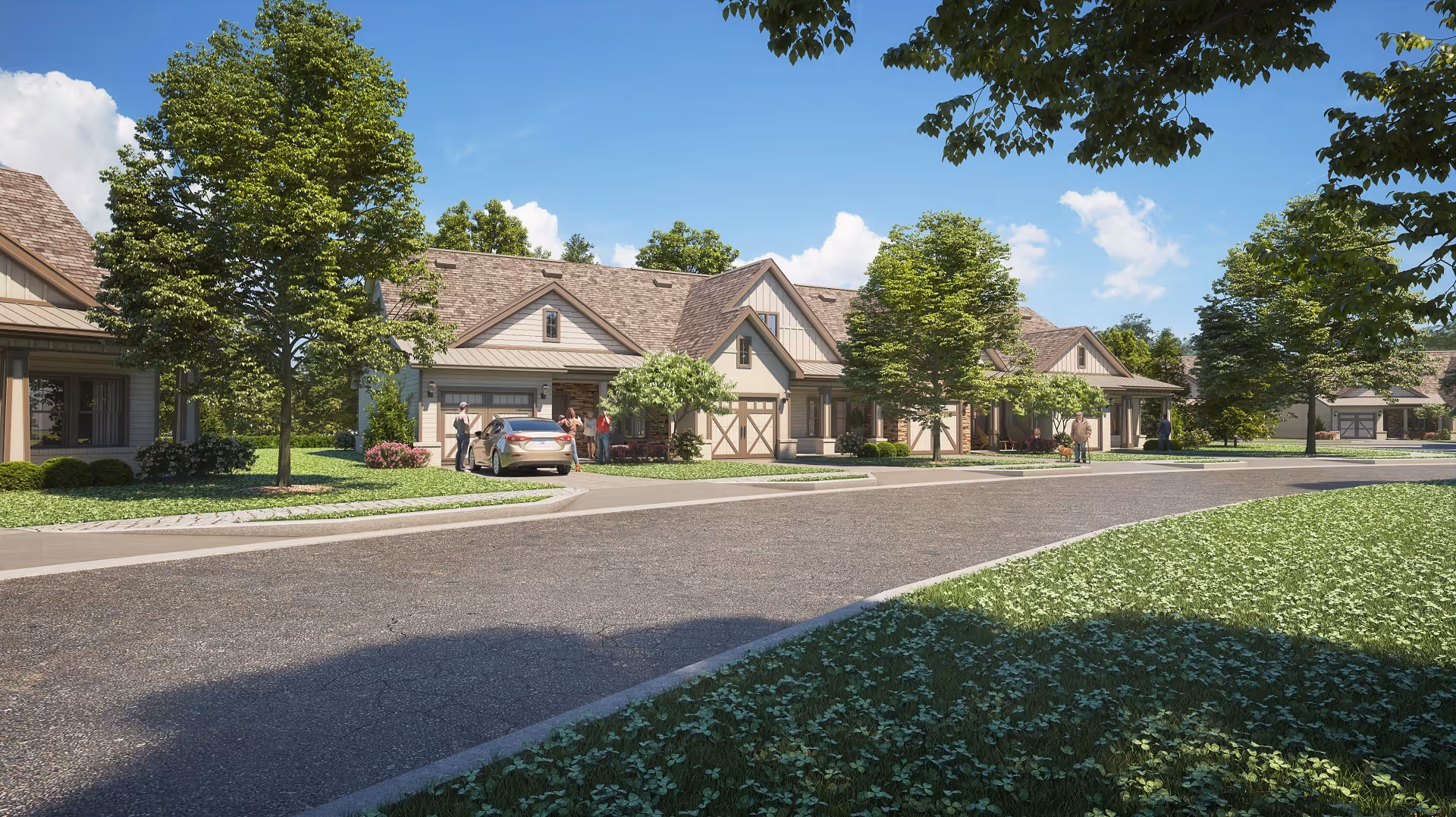 Street view of a residential community with single-story houses featuring pitched roofs and garages. Several trees and well-maintained lawns line the street under a blue sky with some clouds. A few people and a car are visible near the houses.