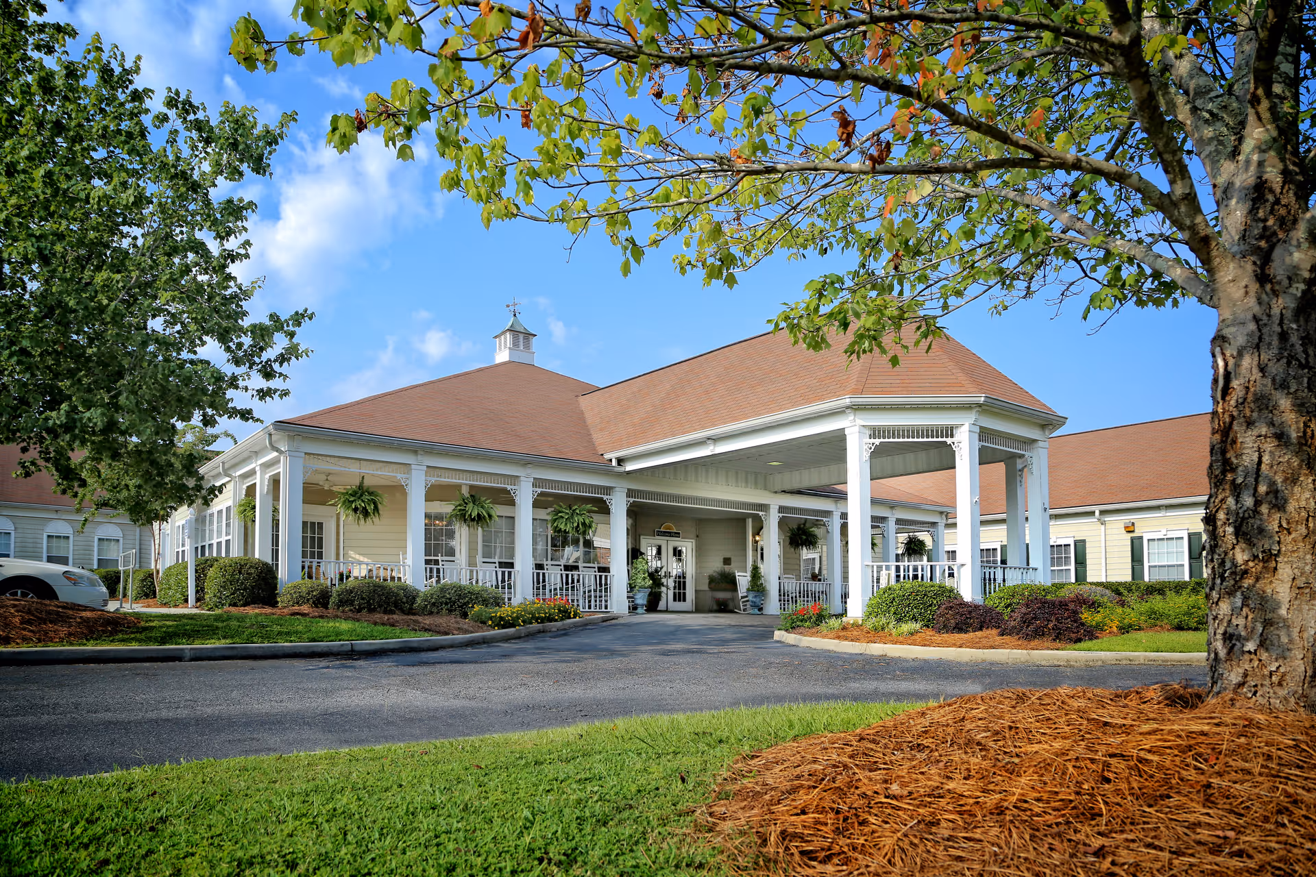 Front entrance of a single-story senior care building with a covered portico, white columns, and landscaped grounds.
