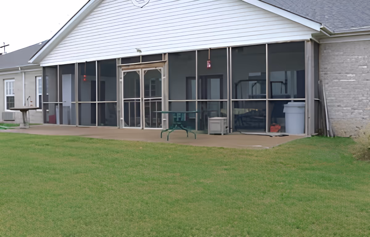 Single-story building with a screened porch and patio facing a grassy lawn.