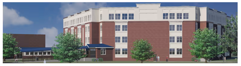 Exterior view of a multi-story senior living facility building with red brick and white accents, surrounded by green trees and a clear blue sky.