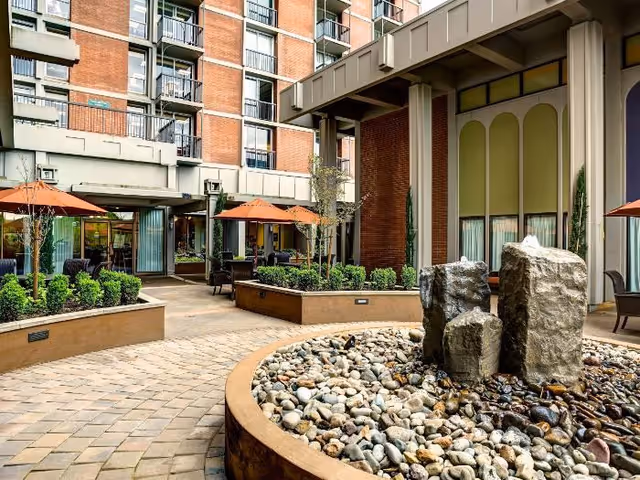 Courtyard patio at Calaroga Terrace with a rock fountain in the foreground, paver walkways, planters and seating areas with orange umbrellas against the building facade.