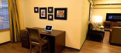 A cozy interior with a desk, laptop, framed art, and lounge area in a senior facility.