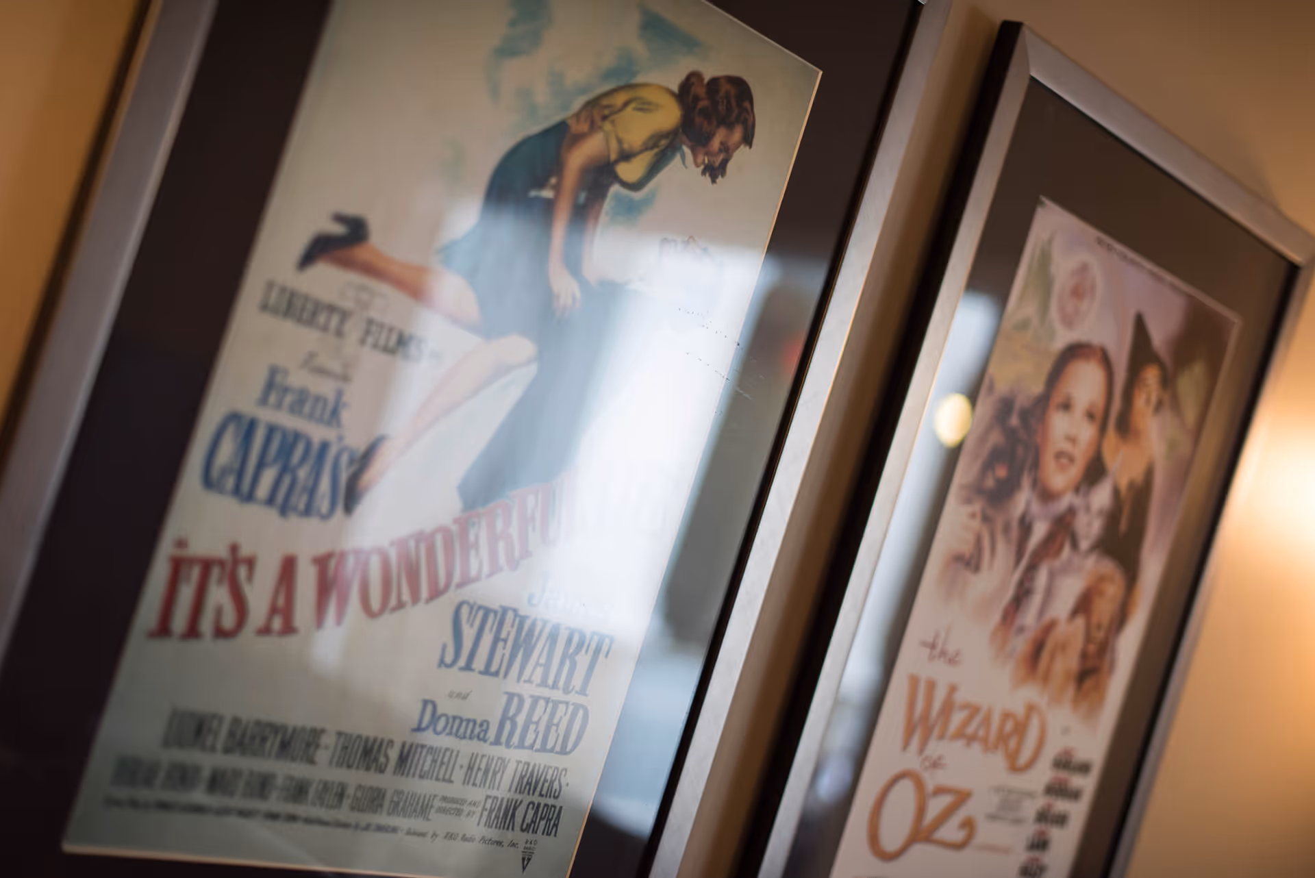 Close-up view of two framed vintage movie posters hanging on a wall. The left poster is for the film 'It's a Wonderful Life' featuring a woman leaning over a man, and the right poster is for 'The Wizard of Oz' showing a young girl with animals.