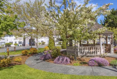 Well-maintained senior living campus exterior featuring a gazebo, paved path, and colorful landscaping.