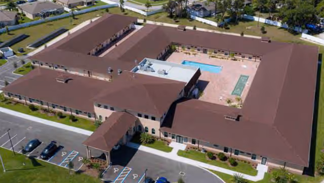 Aerial view of a single-story assisted living complex arranged around a central courtyard with a swimming pool and adjacent parking lot.
