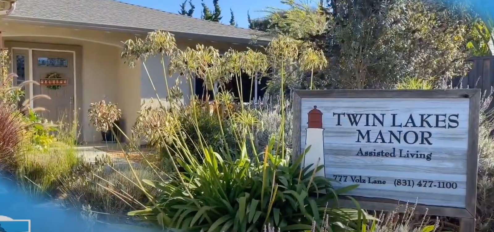 Front entrance and landscaped garden of Twin Lakes Manor assisted living with a wooden sign by the walkway.
