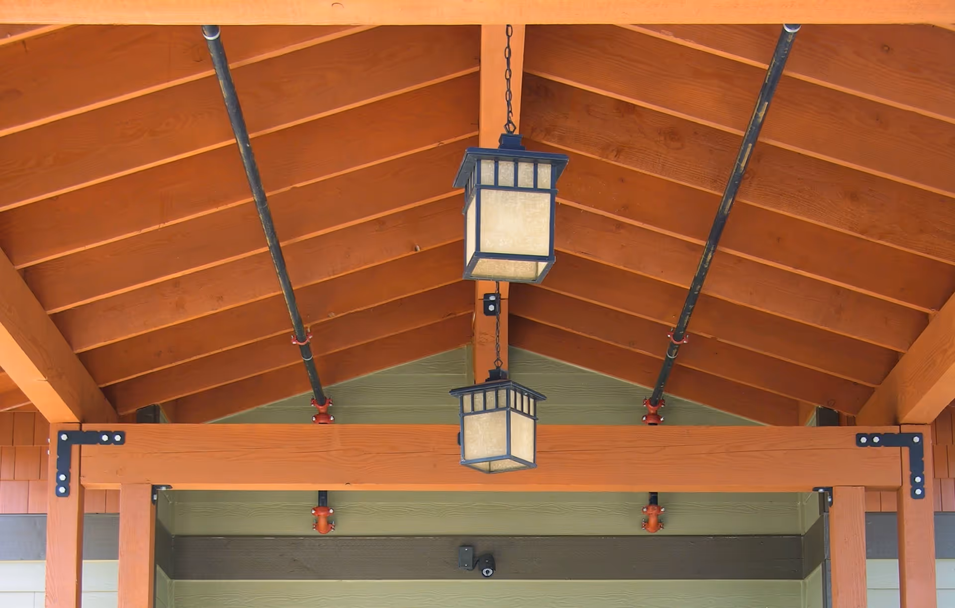 Wooden covered entrance with exposed beams, pipes, and two hanging lantern-style lights.