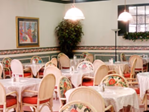 Bright dining room with round tables covered in white tablecloths and floral-upholstered chairs.