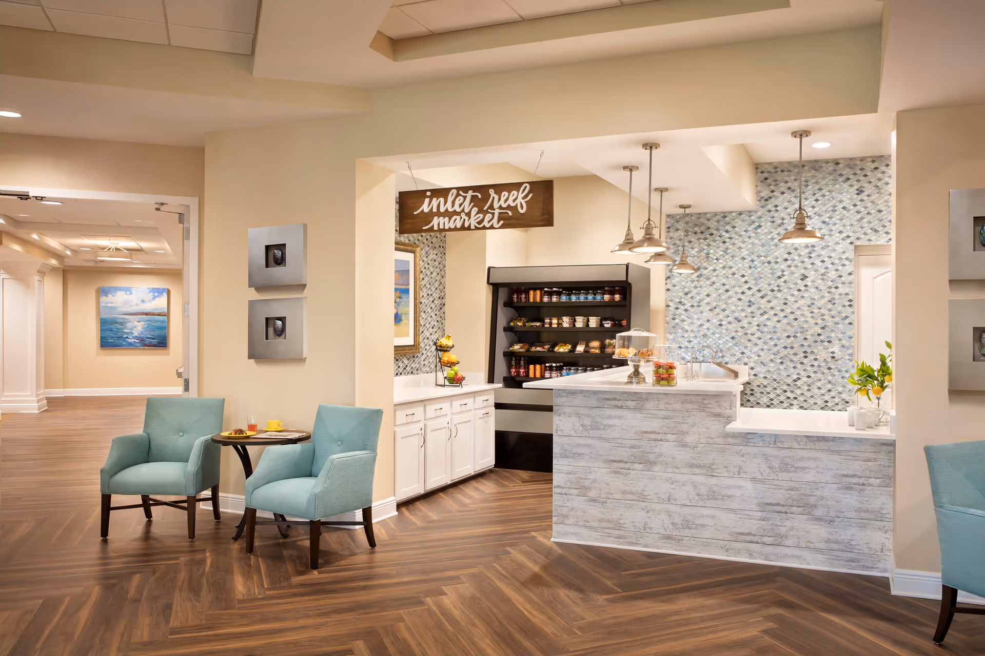Bright interior common area showing a small market counter labeled 'inlet reef market', two teal chairs with a table, and pendant lights.