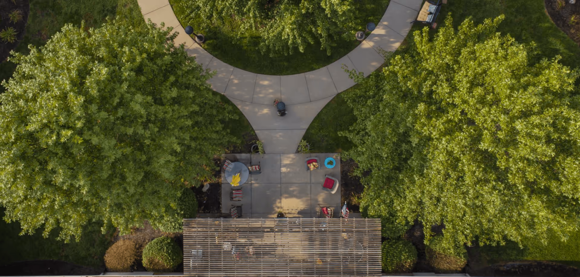 Aerial view of a landscaped courtyard with curved walkways, large trees, and a small seating area with chairs and an umbrella.