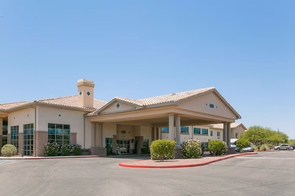 Exterior view of Mountain View Retirement Village building with a covered entrance, beige walls, tiled roof, and surrounding bushes under a clear blue sky.