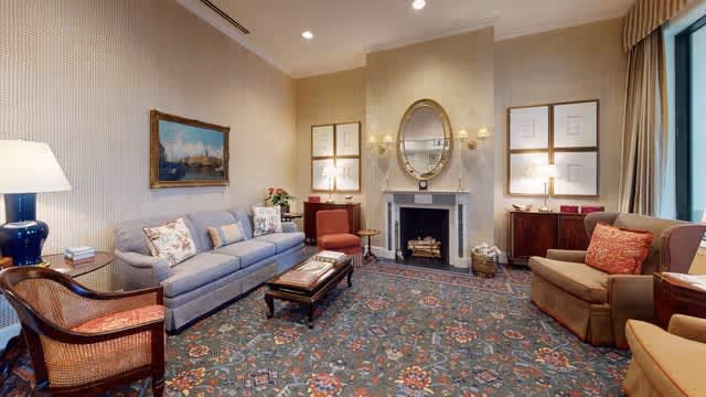 Elegantly furnished communal living room with sofas and armchairs arranged around a fireplace topped by an oval mirror and a patterned carpet.