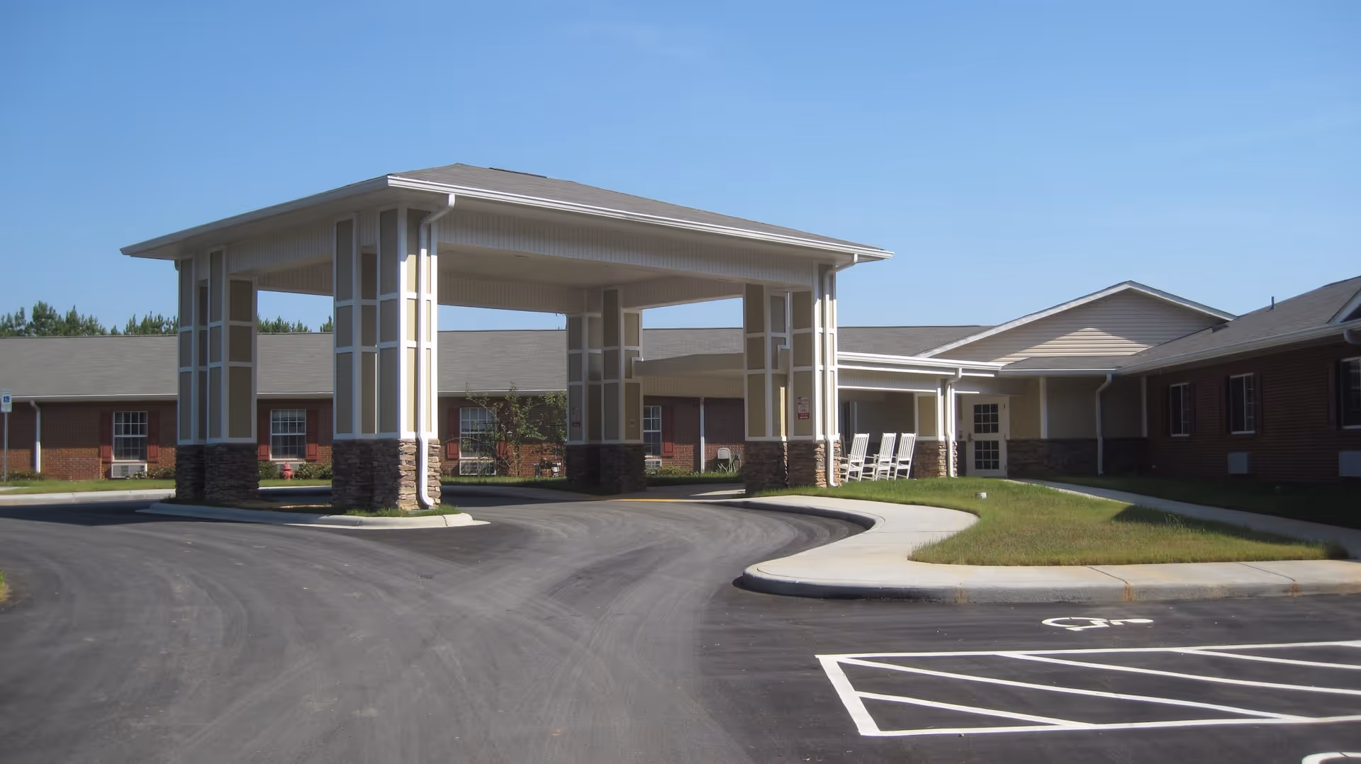 Front exterior view of Woodhaven Court facility showing a covered entrance with large pillars, a curved driveway, and a building with brick and siding under a clear blue sky.