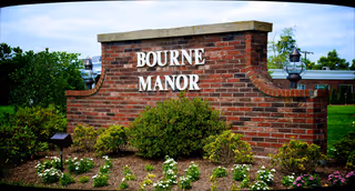 A brick sign reading Bourne Manor sits among shrubs at the facility's outdoor entrance.