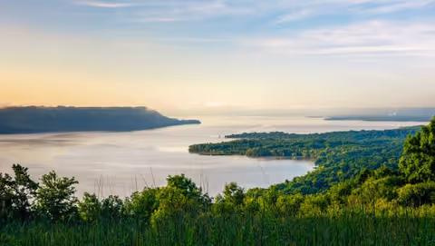Scenic view of a large body of water surrounded by lush green trees and hills under a partly cloudy sky during daylight.
