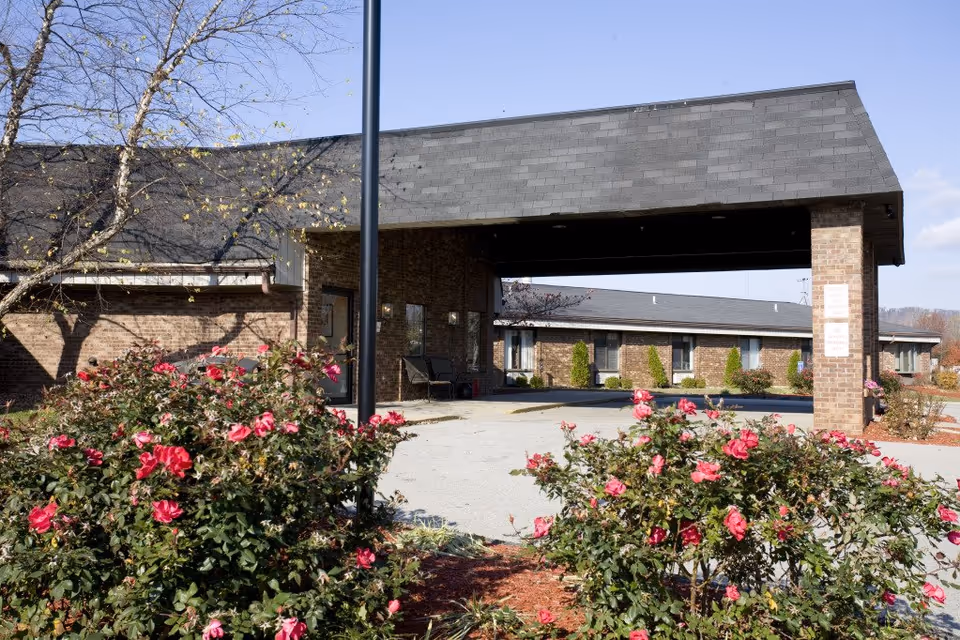 Covered entrance of a brick healthcare building with flowering bushes in the foreground.